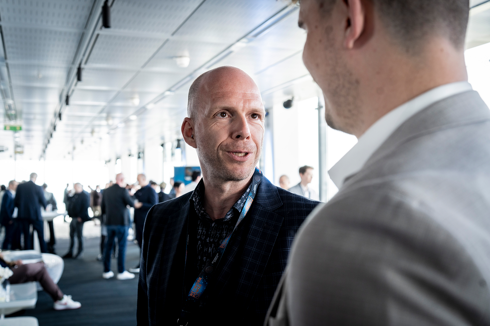 Two men engaged in conversation at a professional event, surrounded by attendees and event decor.