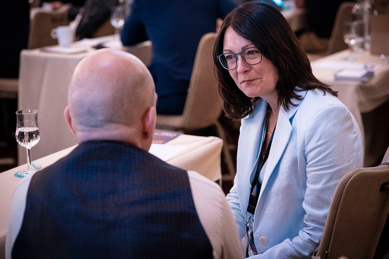 A woman and a man engaged in conversation at a table, with the woman actively speaking.