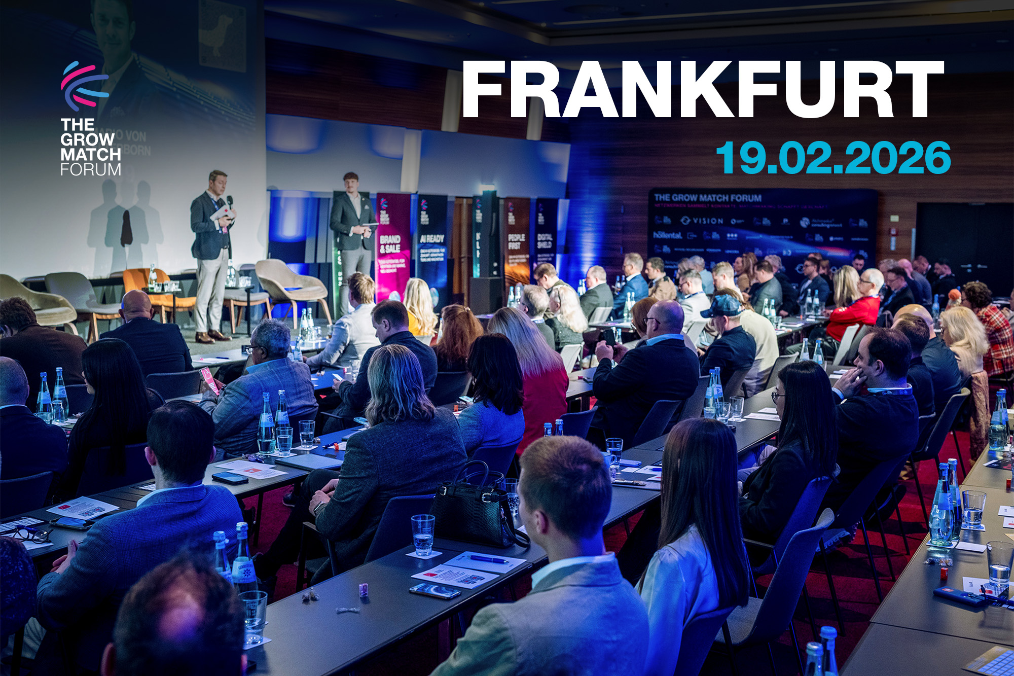 Smiling woman with curly hair at a formal dinner table, wearing a smartwatch. Background shows people in conversation, wine glasses, and bottled water.